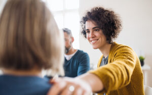 A woman extends her arm to hold another person's shoulder in a group discussion.