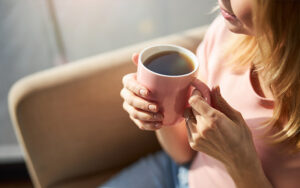 A person is sitting looking out the window, holding a cup of coffee.