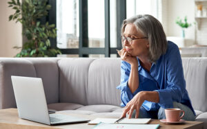 An elder woman is sitting on her couch reading her laptop.