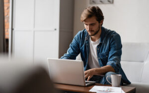 A young man sitting and reading his laptop.