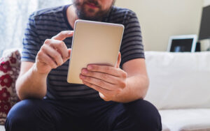 A young man sitting on a couch reading a tablet.