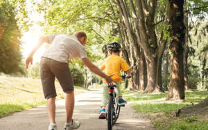 A man is helping to teach their child how to ride a bike. He is about to let go and allow the child to pedal on their own.