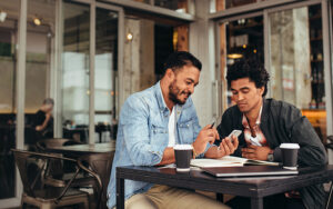 Two men at a cafe looking at a phone and taking notes.