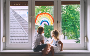 Two children sitting on a windowsill. On the window a rainbow has been painted.