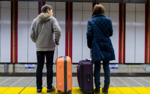 Two people with suitcases standing on a train platform.