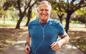 An elder man is running in the park and listening to music with a smile on his face.