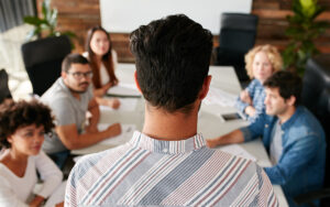 A man is looking down at the people sitting at a table.