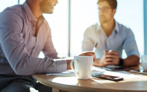 Two men sitting at a table and talking to one another.