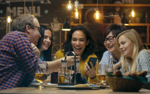 A group of people at a bar laughing and looking at their phones.