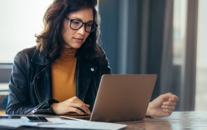 A woman wearing glasses reading her laptop.