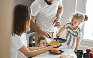 A family eating a pancake breakfast together. We do not see the parents faces, and the camera feels like it's "peeking" in on this moment for the family.