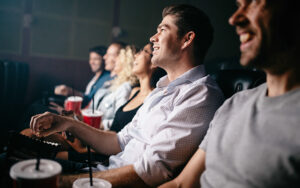 A group of people are at sitting watching a movie at the movie theatre. It's dark and a person's hand is raised as if they were about to "make a move".