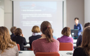 A group of people are sitting and watching a lecture take place.
