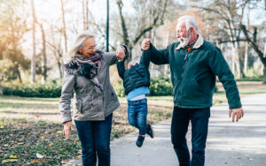 An elder grandmother and grandfather are playing with a young child while in the park.